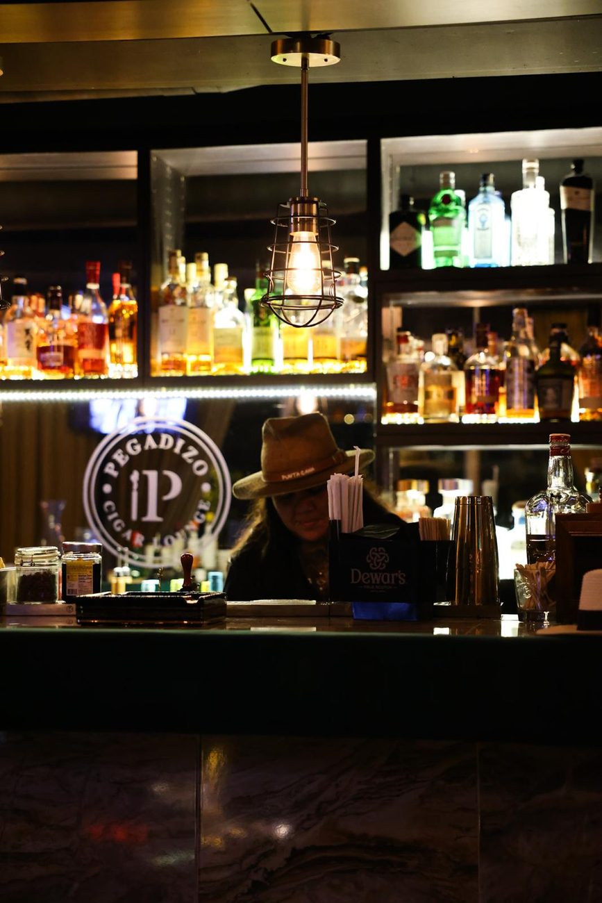 La barra de Pegadizo, con la estanteria de botellas iluminada y el logo detras