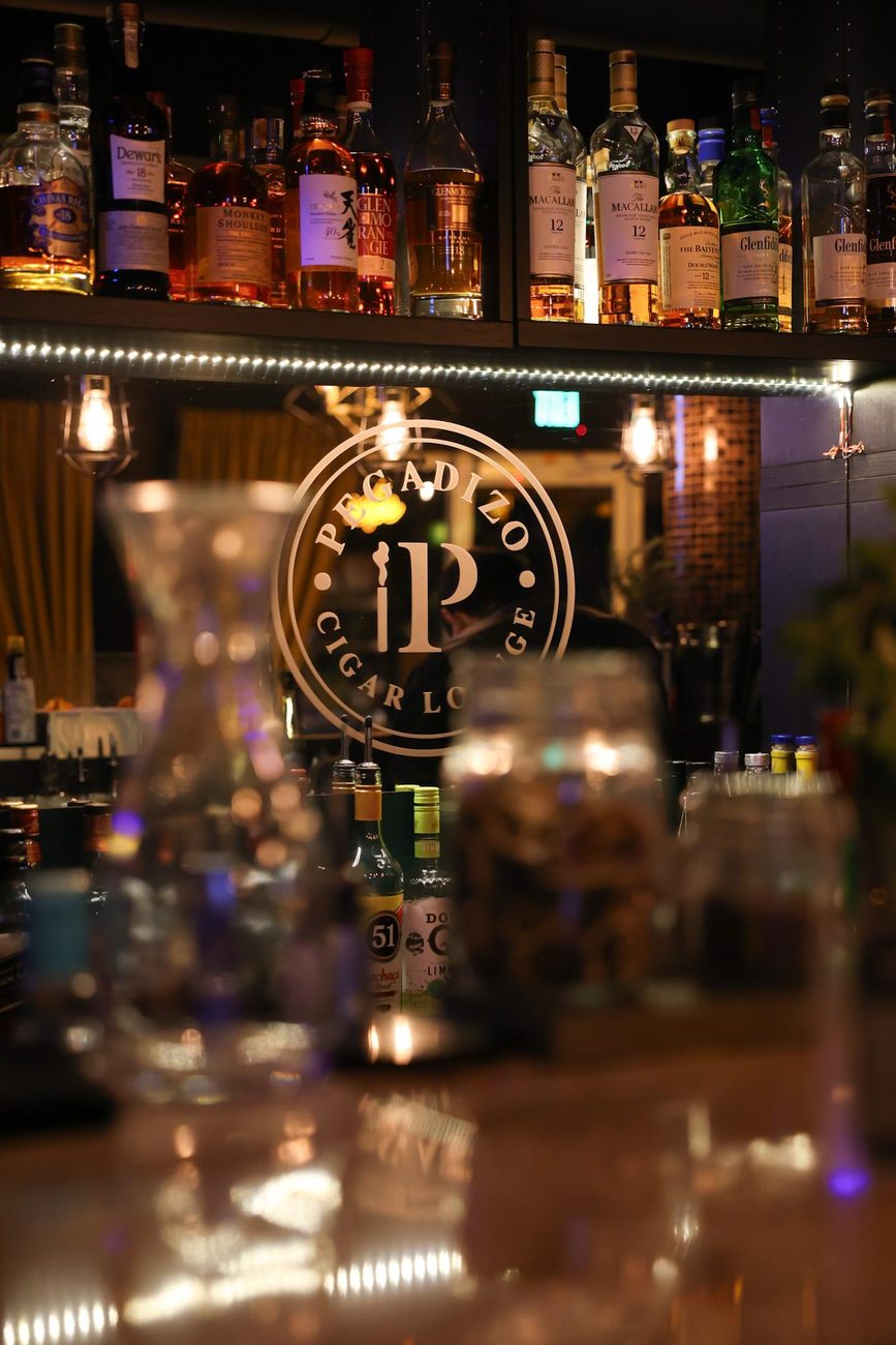 La pared de botellas del bar, con el logo P de Pegadizo al frente