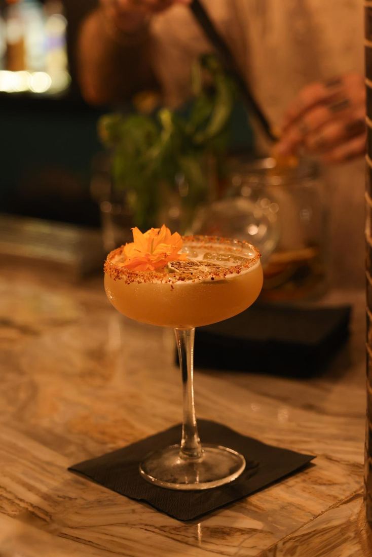 Un coctel de autor en copa, con guarnicion, sobre la barra de marmol