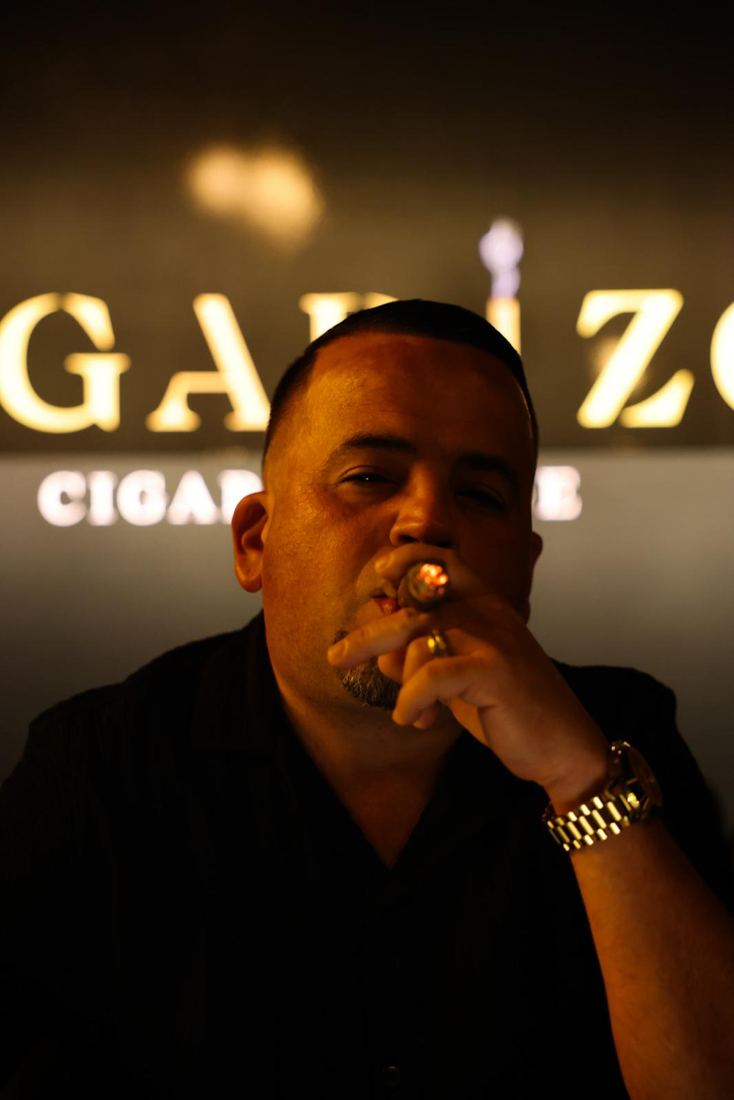 Un cliente fumando un cigarro debajo del letrero iluminado de Pegadizo