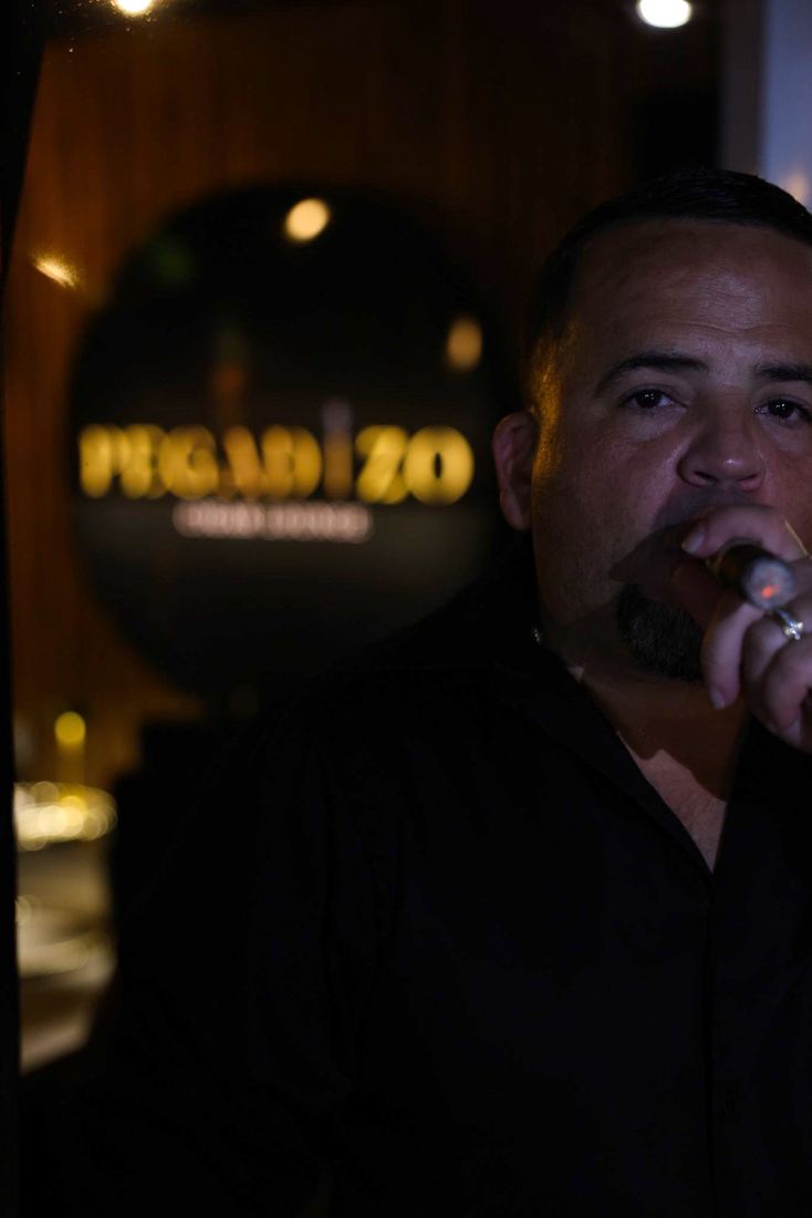 Un cliente con un cigarro frente al letrero de Pegadizo Cigar Lounge