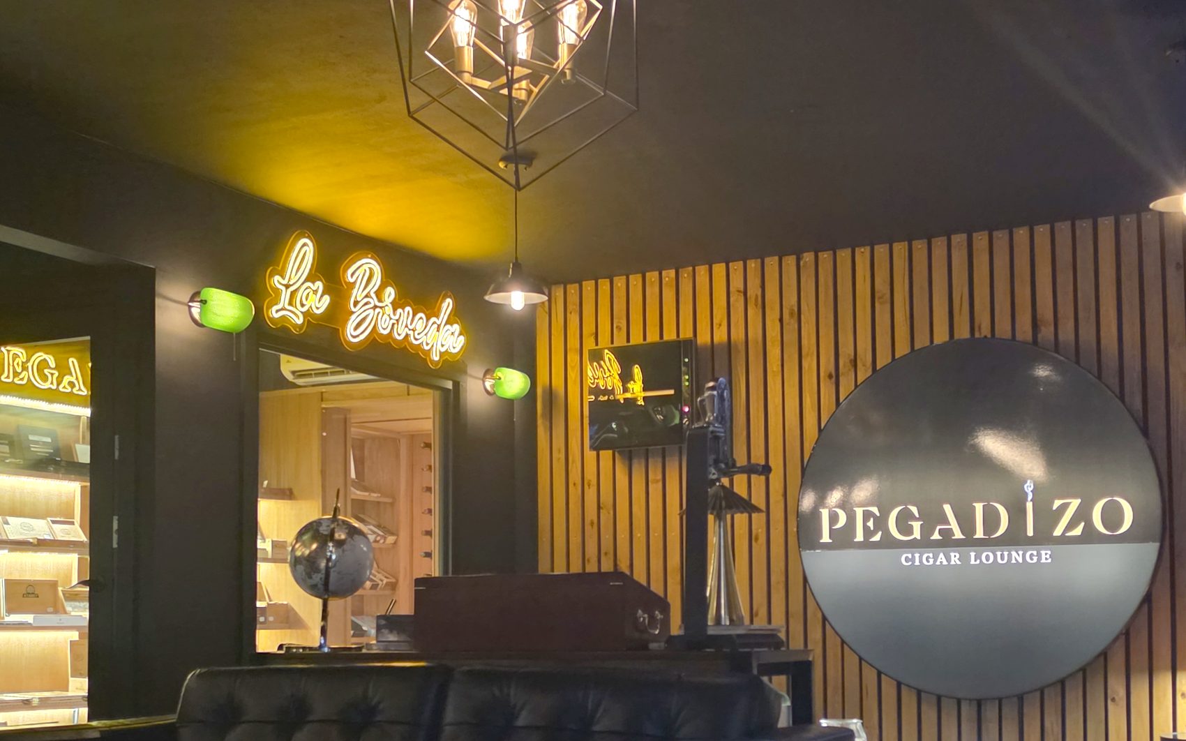 El letrero redondo de Pegadizo Cigar Lounge sobre la pared de listones de cedro